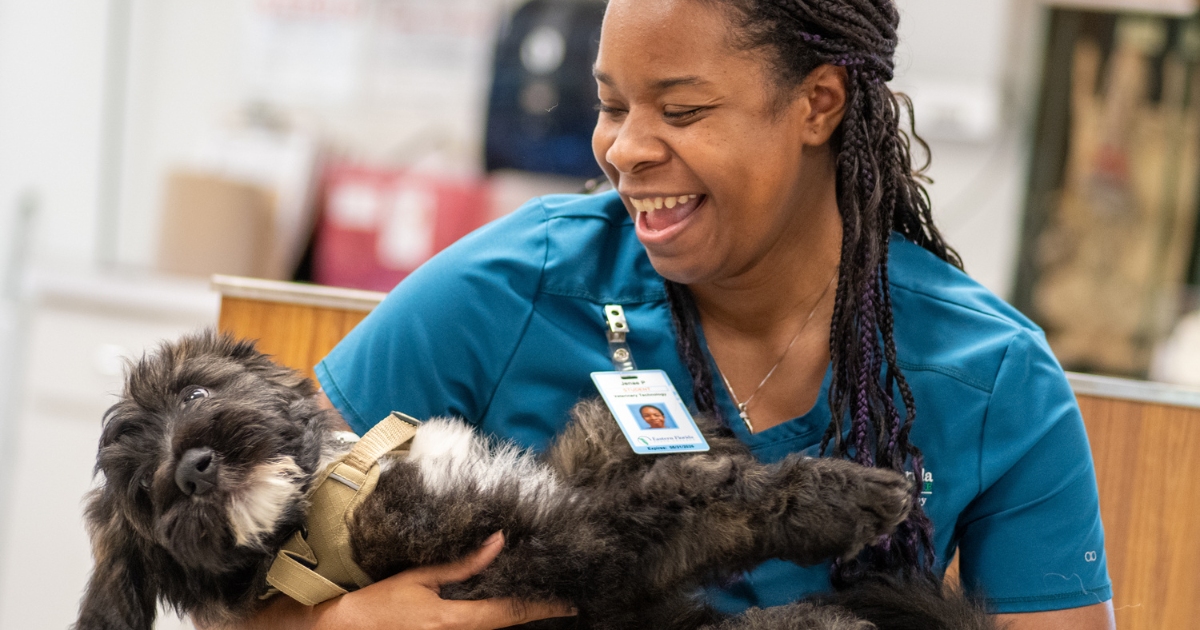 A student is smiling while holding a dog in her lap