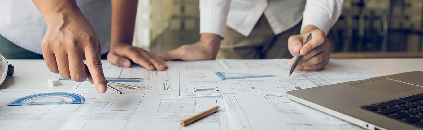 Two people pointing to blueprints spread out on a table.